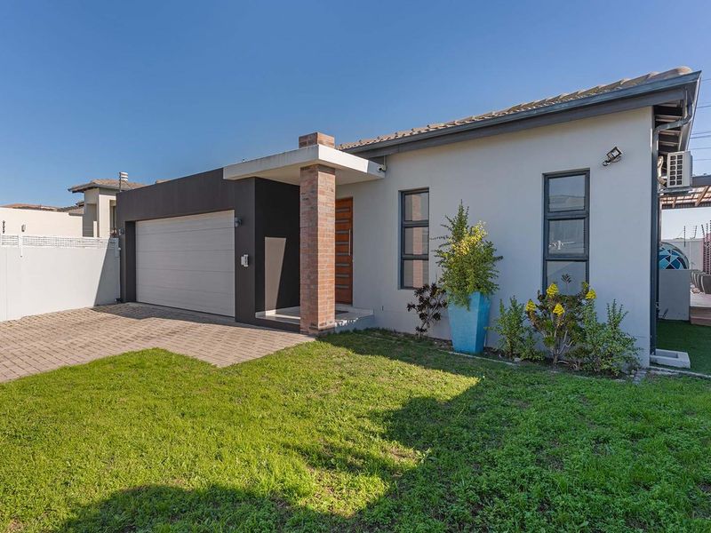 Modern front elevation featuring a paved driveway, single garage, and a distinctive brick pillar entrance, set against a well-maintained lawn.