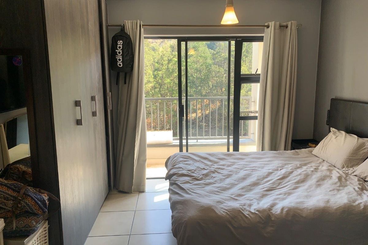 A bedroom featuring built-in cupboards, tiled flooring, and a sliding glass door providing access to a private balcony with a scenic view.