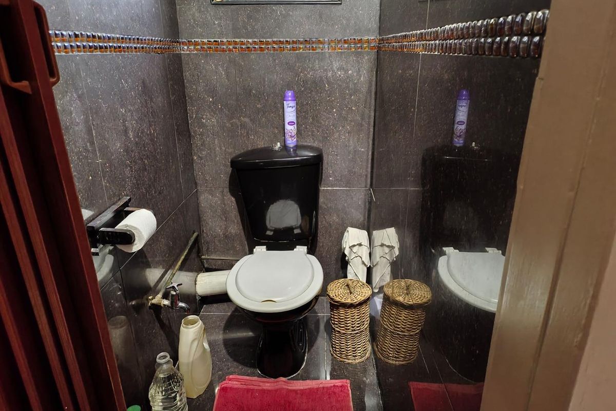 A compact bathroom featuring dark wall and floor tiles, a black toilet, and an exposed plumbing pipe.