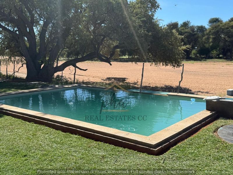 Outdoor swimming pool set within a garden area, featuring stone coping and a brick surround, overlooking open farm land.