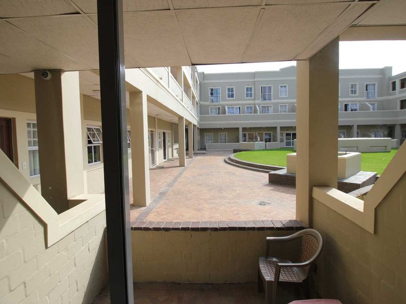 A covered balcony overlooking a well-maintained communal courtyard with brick paving and landscaped garden areas within the apartment complex.