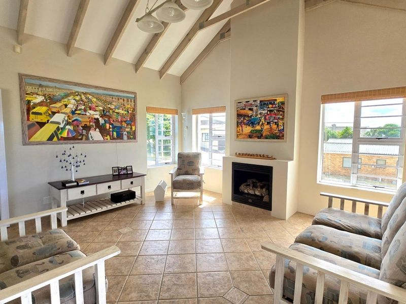 Spacious living room featuring a vaulted ceiling with exposed timber beams, tiled flooring, and a built-in fireplace, offering a bright and airy atmosphere.