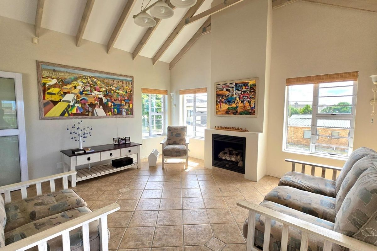 Spacious living room featuring a vaulted ceiling with exposed timber beams, tiled flooring, and a built-in fireplace, offering a bright and airy atmosphere.