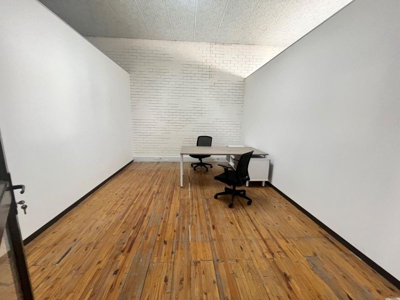 A minimalist office space featuring exposed white brick walls, original hardwood flooring, and acoustic ceiling tiles, offering a clean and functional workspace.