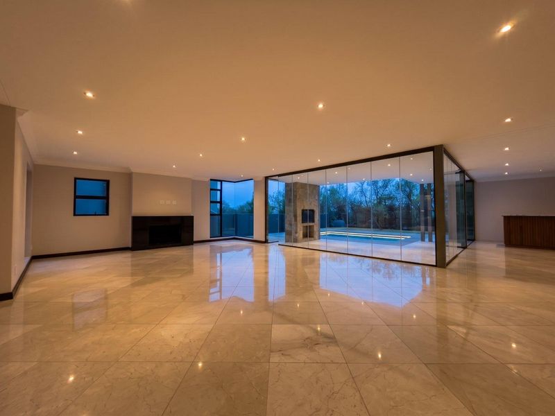 Spacious open-plan living area featuring polished marble flooring, recessed lighting, a built-in fireplace, and expansive glass walls overlooking the pool area.