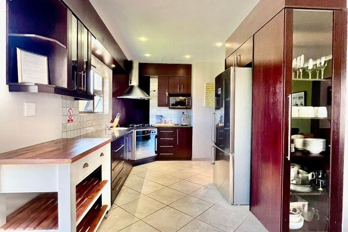 A well-maintained kitchen featuring dark wood cabinetry, tiled flooring, a stainless steel extractor fan, and integrated display shelving.