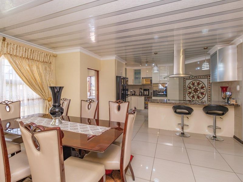 Spacious open-plan dining and kitchen area featuring tiled flooring, granite countertops, a breakfast bar, and a modern stainless steel extractor fan.