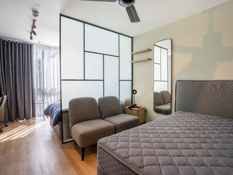 A modern bedroom featuring laminate flooring, a sleek glass room divider, built-in wardrobe storage, and contemporary track lighting.