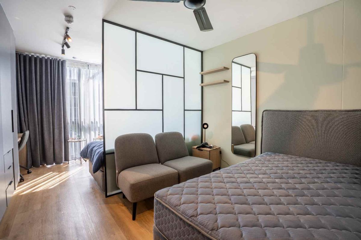 A modern bedroom featuring laminate flooring, a sleek glass room divider, built-in wardrobe storage, and contemporary track lighting.