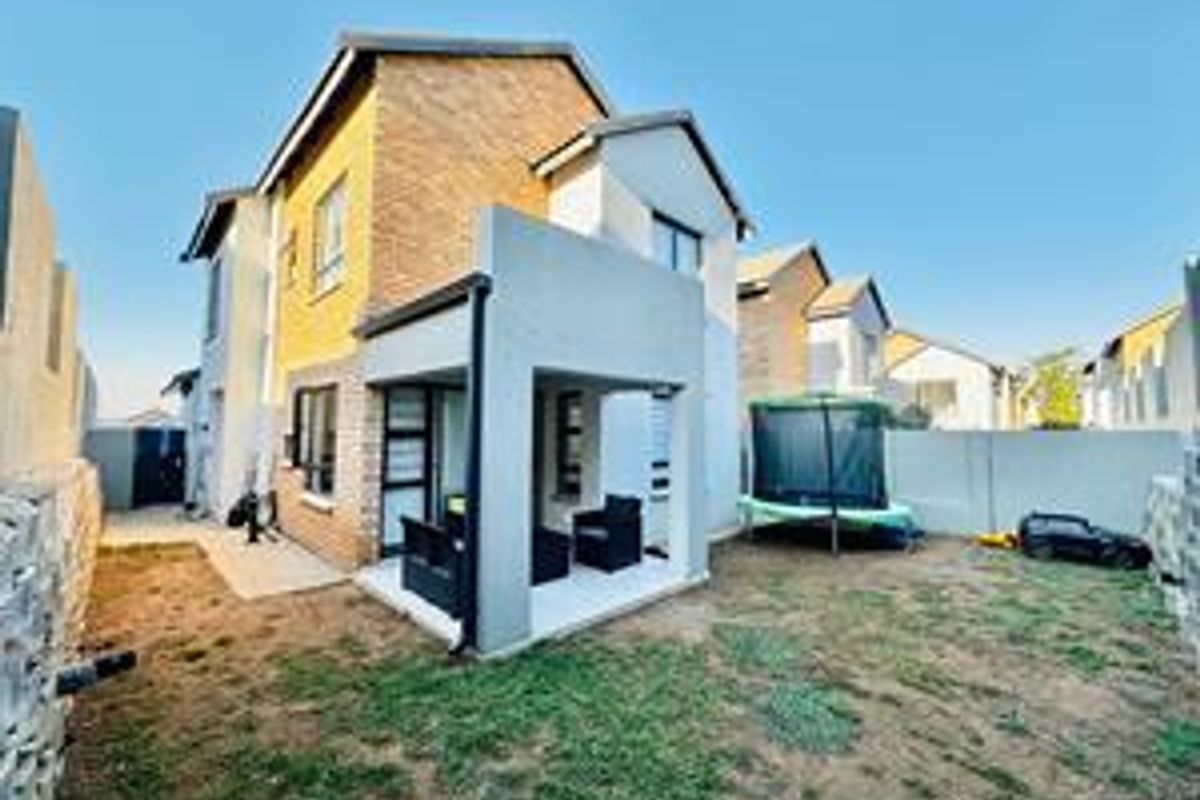 Rear view of a double-story cluster home featuring a covered patio, brick and plaster facade, and a private garden area.