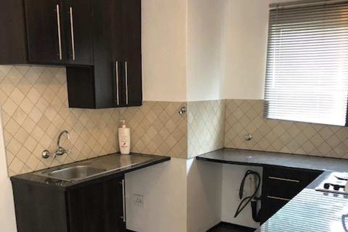 A functional kitchen featuring dark cabinetry, granite countertops, a stainless steel sink, and tiled splashbacks with a window providing natural light.