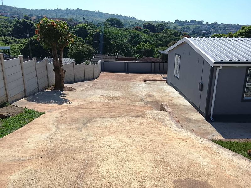 A spacious rear exterior area featuring a large concrete driveway, enclosed by precast boundary walls, with views of the surrounding landscape.