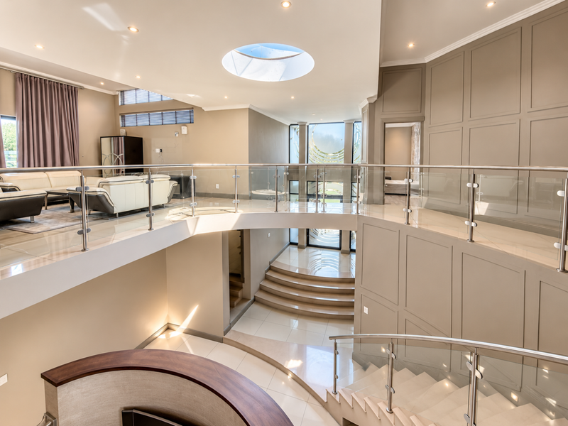 Spacious double-volume entrance hall featuring a grand curved staircase, glass balustrades, elegant wall paneling, and a circular skylight providing natural light.