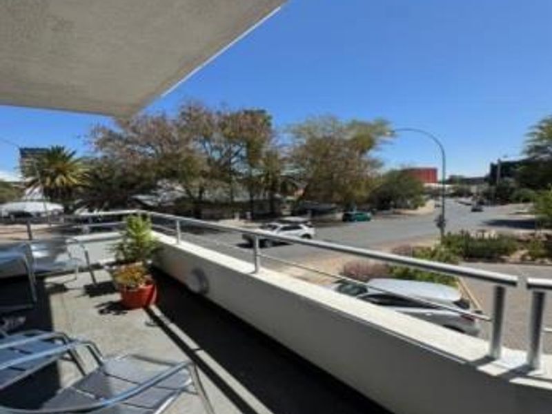 A spacious balcony featuring a metal safety railing and concrete flooring, offering an elevated view of the surrounding street and neighborhood.