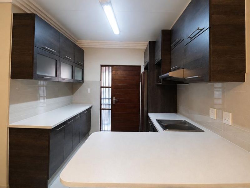 Modern kitchen featuring dark wood cabinetry, white stone countertops, built-in hob, extractor fan, and tiled flooring with a clean, functional layout.