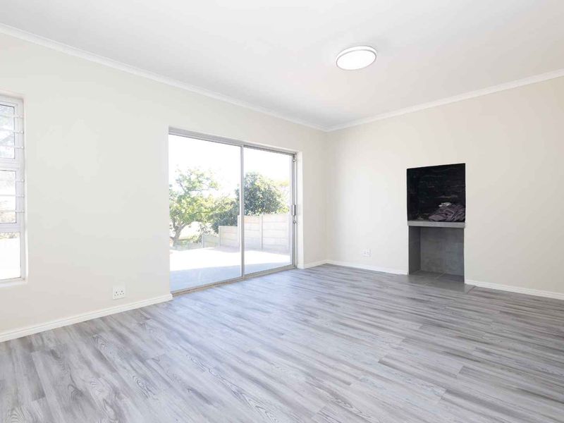 A bright, empty living room featuring modern laminate flooring, a built-in fireplace, and a large sliding glass door providing access to the outdoor area.