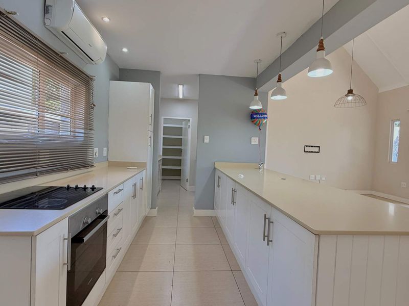 Spacious open-plan kitchen featuring modern white cabinetry, stone countertops, integrated appliances, and seamless flow to the adjacent living area and outdoor patio.