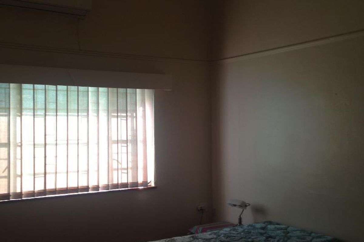 A bedroom featuring a ceiling fan, wall-mounted air conditioning unit, and vertical window blinds.
