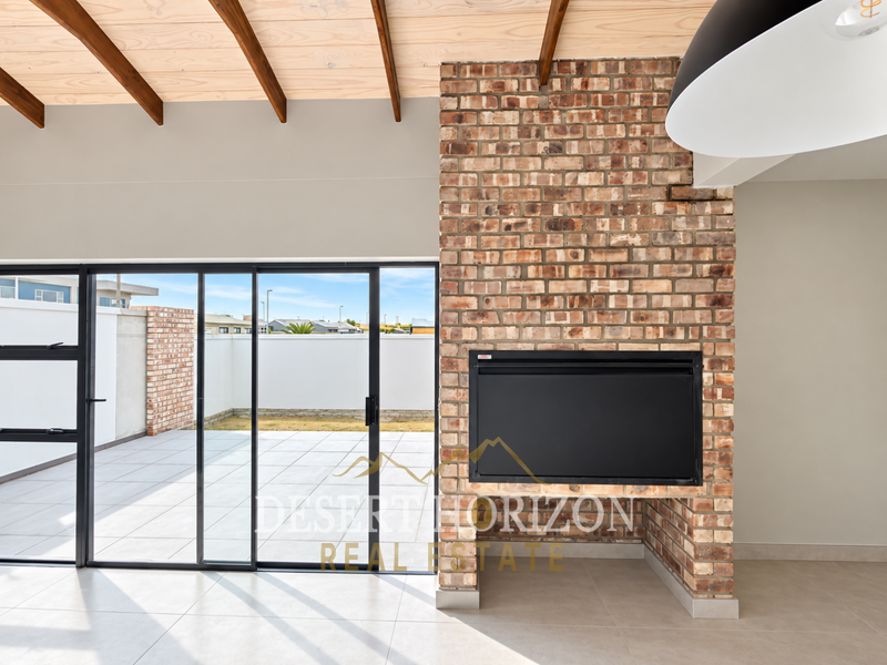 Spacious living area featuring an exposed brick fireplace, timber ceiling beams, and large sliding glass doors opening onto a paved patio.