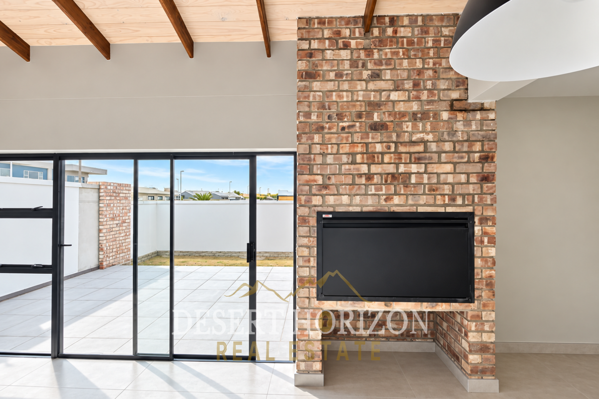 Spacious living area featuring an exposed brick fireplace, timber ceiling beams, and large sliding glass doors opening onto a paved patio.
