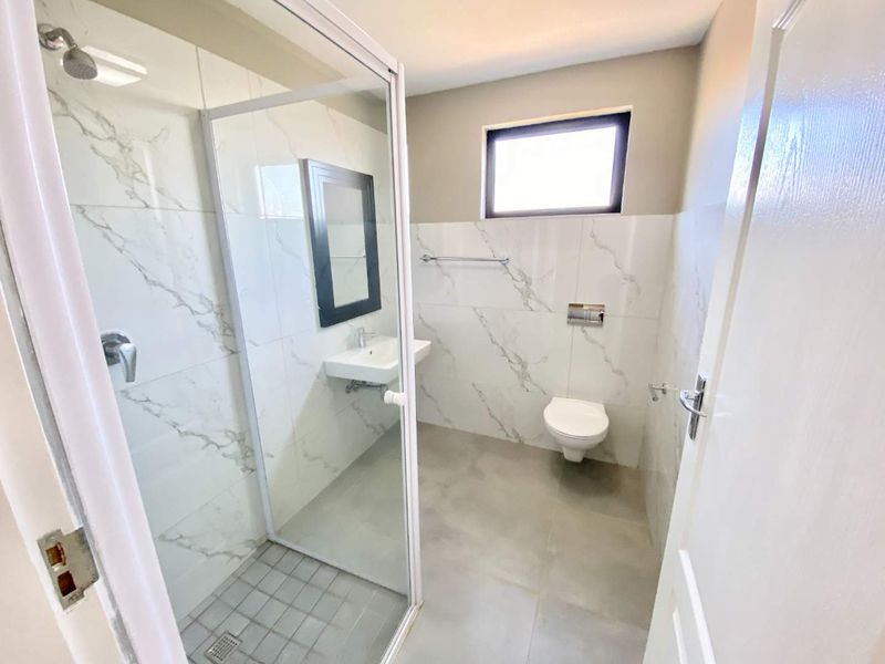 Modern bathroom featuring a wall-mounted toilet, glass shower enclosure, and elegant marble-look wall tiling in a clean, minimalist layout.