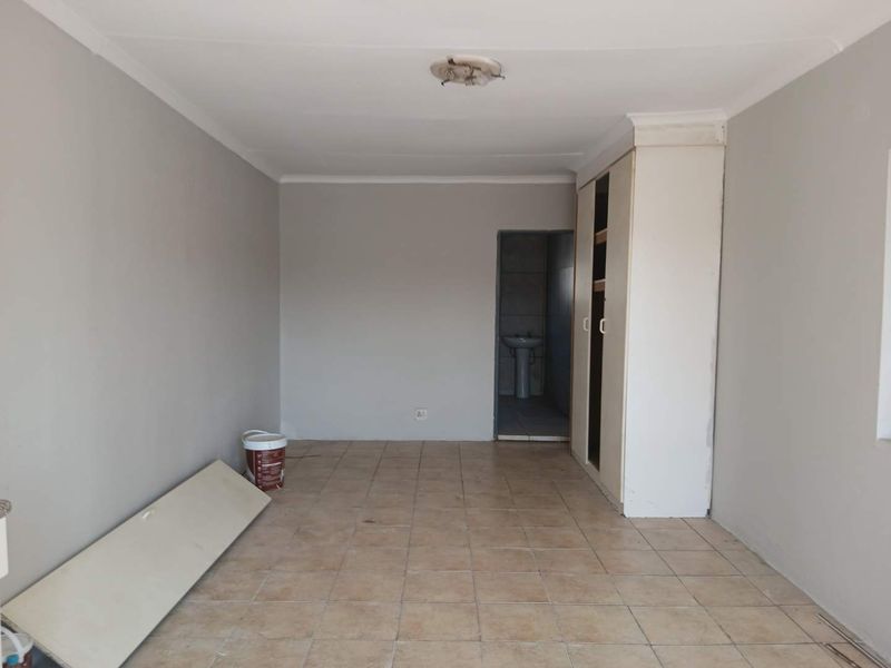 An empty bedroom featuring tiled flooring, a built-in wardrobe with a missing door, and access to an adjoining bathroom area.