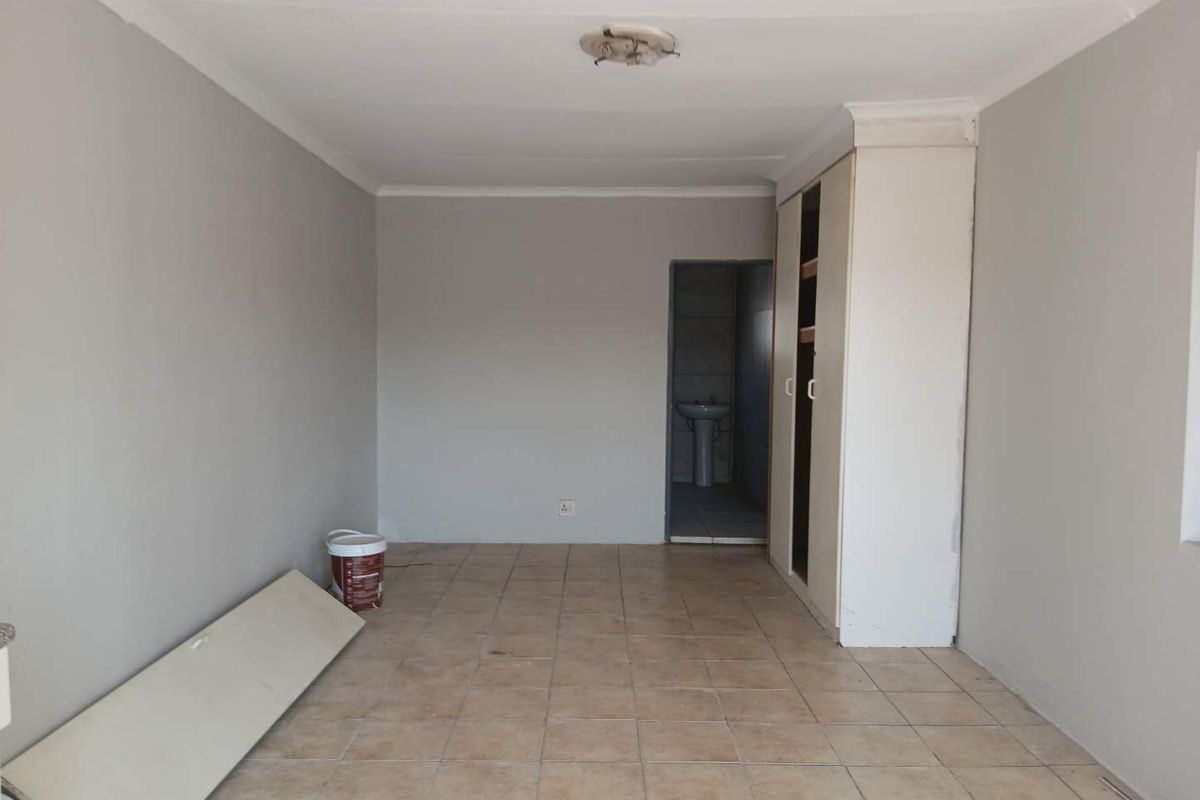 An empty bedroom featuring tiled flooring, a built-in wardrobe with a missing door, and access to an adjoining bathroom area.