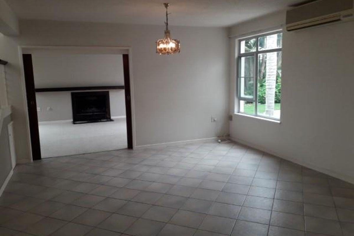 Spacious living area featuring neutral tiled flooring, a wall-mounted air conditioning unit, and an open transition to an adjacent room with a fireplace.