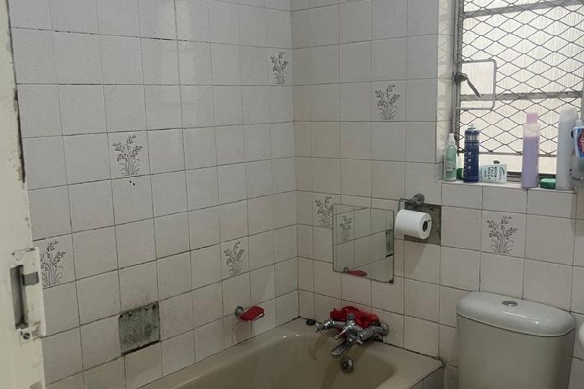 A dated bathroom featuring a bathtub, toilet, and wall-mounted tiling with a security-grille window.
