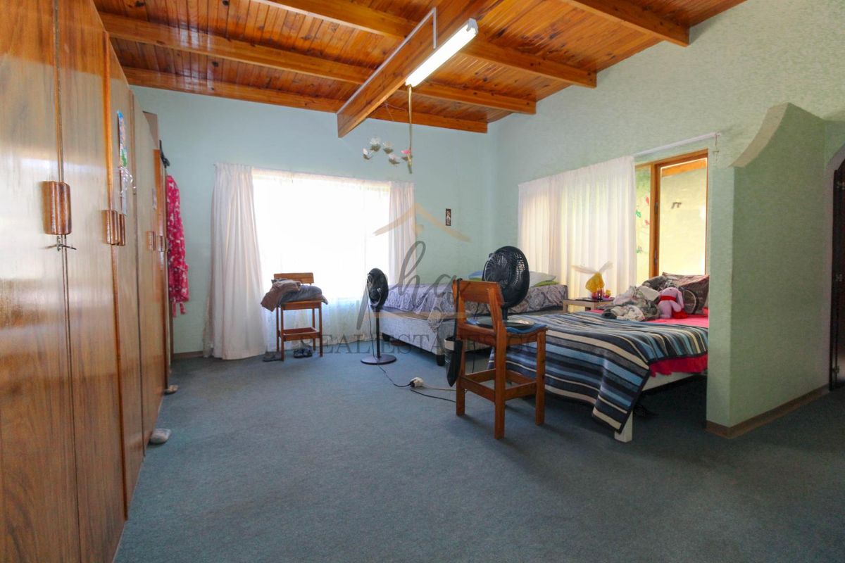 Spacious bedroom featuring exposed timber beam ceiling, built-in wooden cabinetry, and carpeted flooring with direct access to an outdoor area.