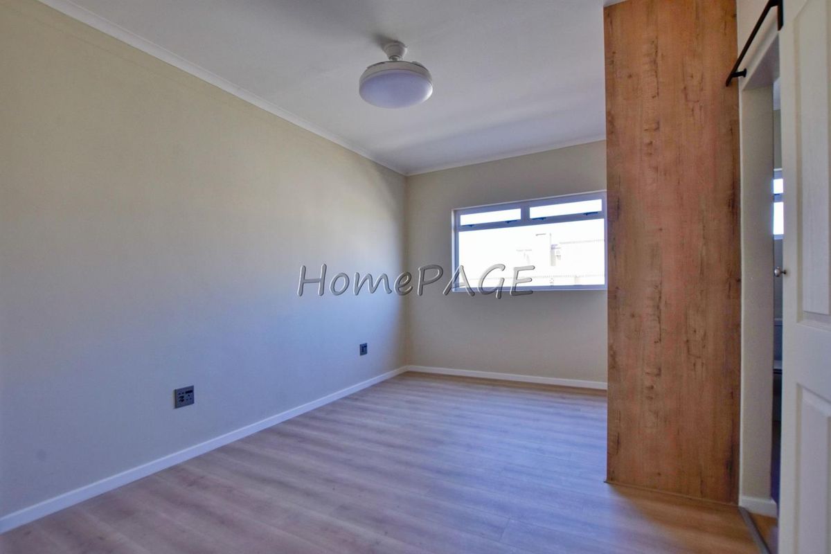 A bright, empty bedroom featuring modern wood-look laminate flooring, neutral wall tones, and a built-in wooden partition.