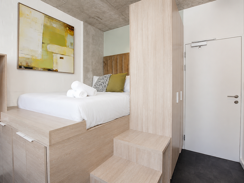 Modern bedroom featuring a custom built-in bed platform with integrated storage, a matching wardrobe, and an exposed concrete ceiling for a contemporary industrial aesthetic.