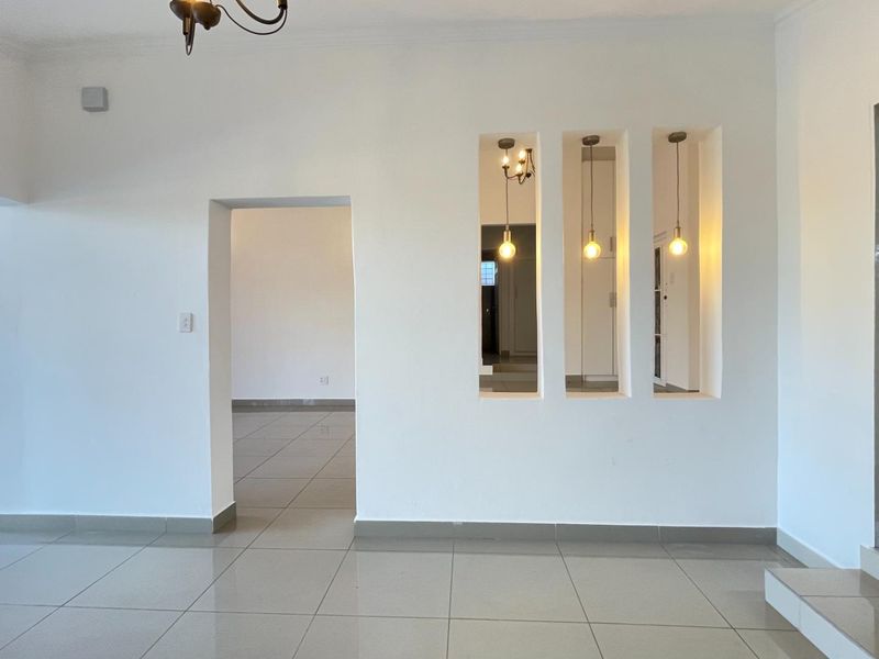 An open-plan living area featuring neutral tiled flooring, decorative wall niches with pendant lighting, and a secure entrance gate.
