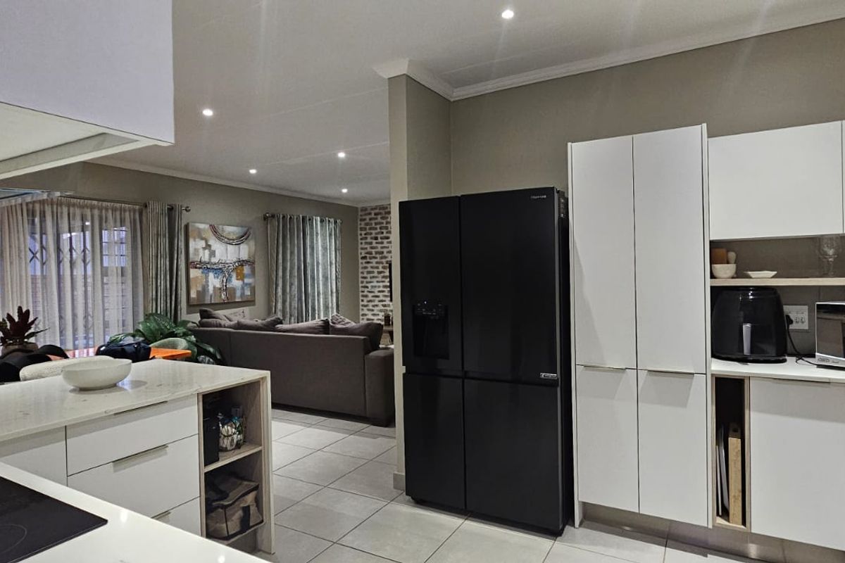 Modern open-plan kitchen featuring sleek white cabinetry, stone countertops, and integrated appliances, flowing seamlessly into a comfortable living area with tiled floors.