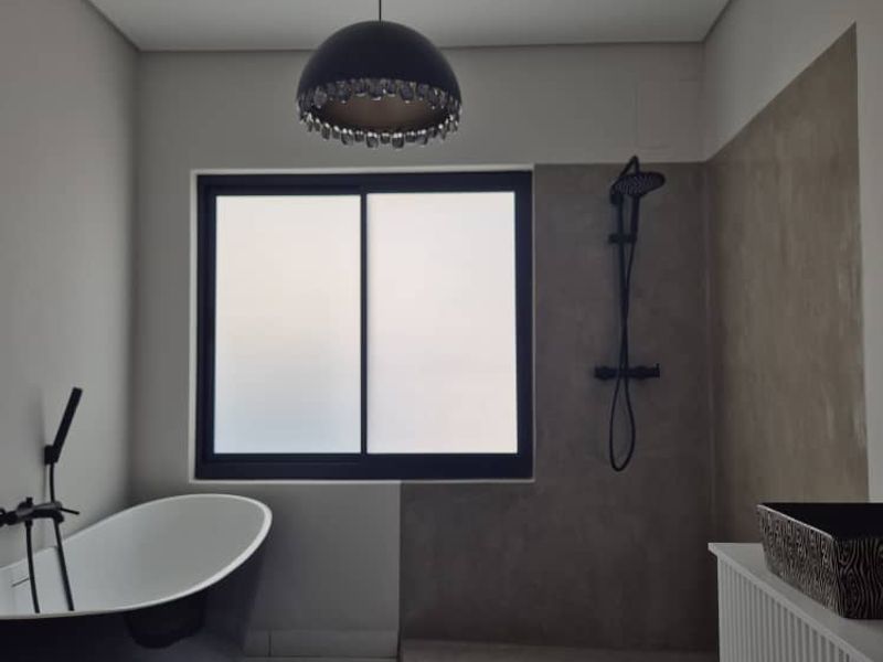 Modern bathroom featuring a sleek freestanding bathtub, a walk-in shower with concrete-look finishes, and contemporary black fixtures.