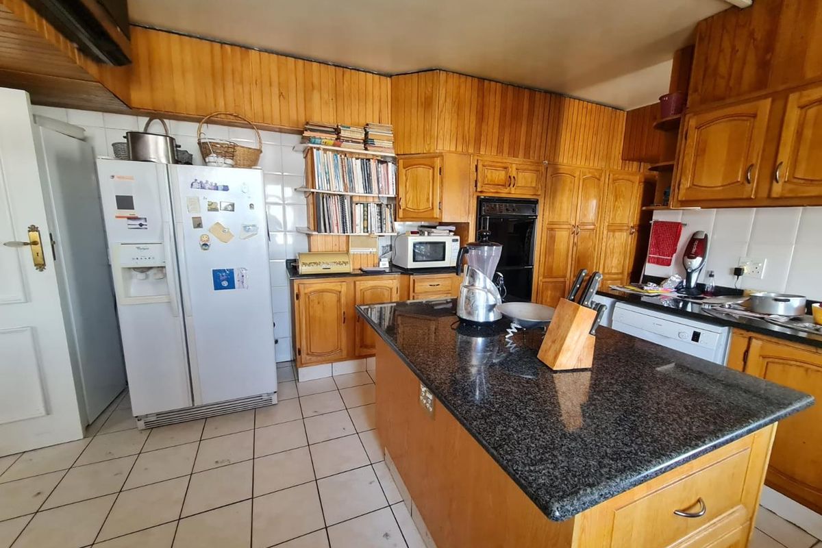 A dated kitchen featuring extensive wood cabinetry, a central island with a granite countertop, built-in oven, and tiled flooring.