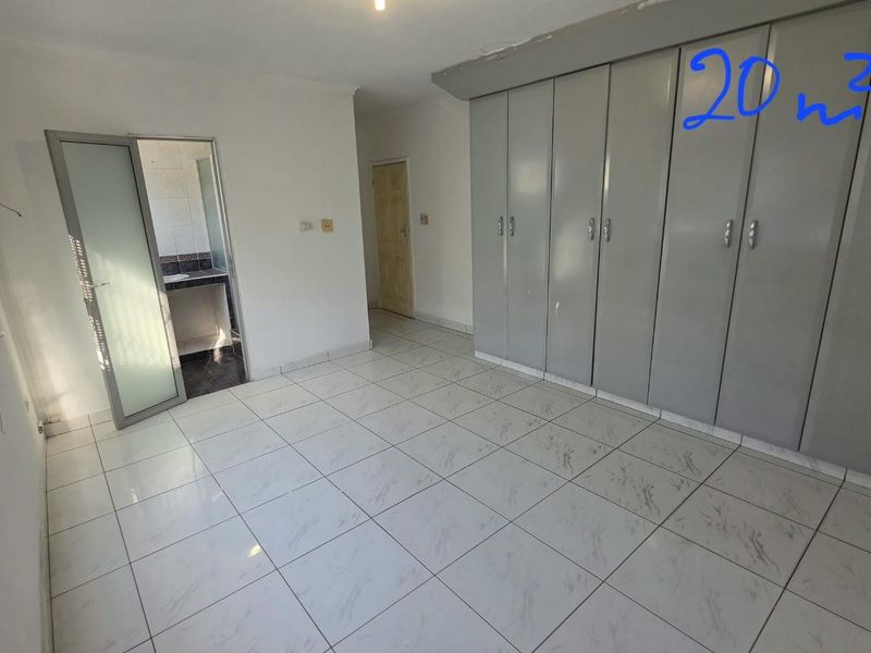 Spacious office area featuring tiled flooring, extensive built-in storage cupboards, and an adjoining bathroom, providing a functional workspace environment.