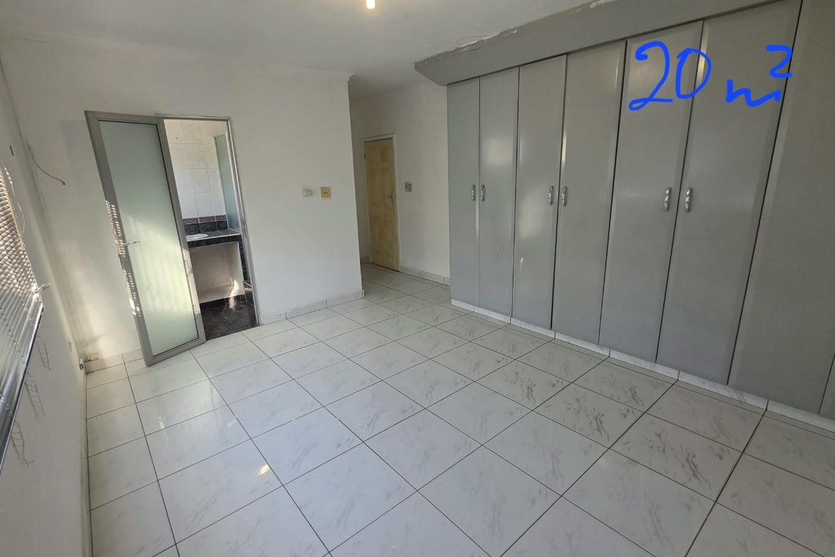 Spacious office area featuring tiled flooring, extensive built-in storage cupboards, and an adjoining bathroom, providing a functional workspace environment.