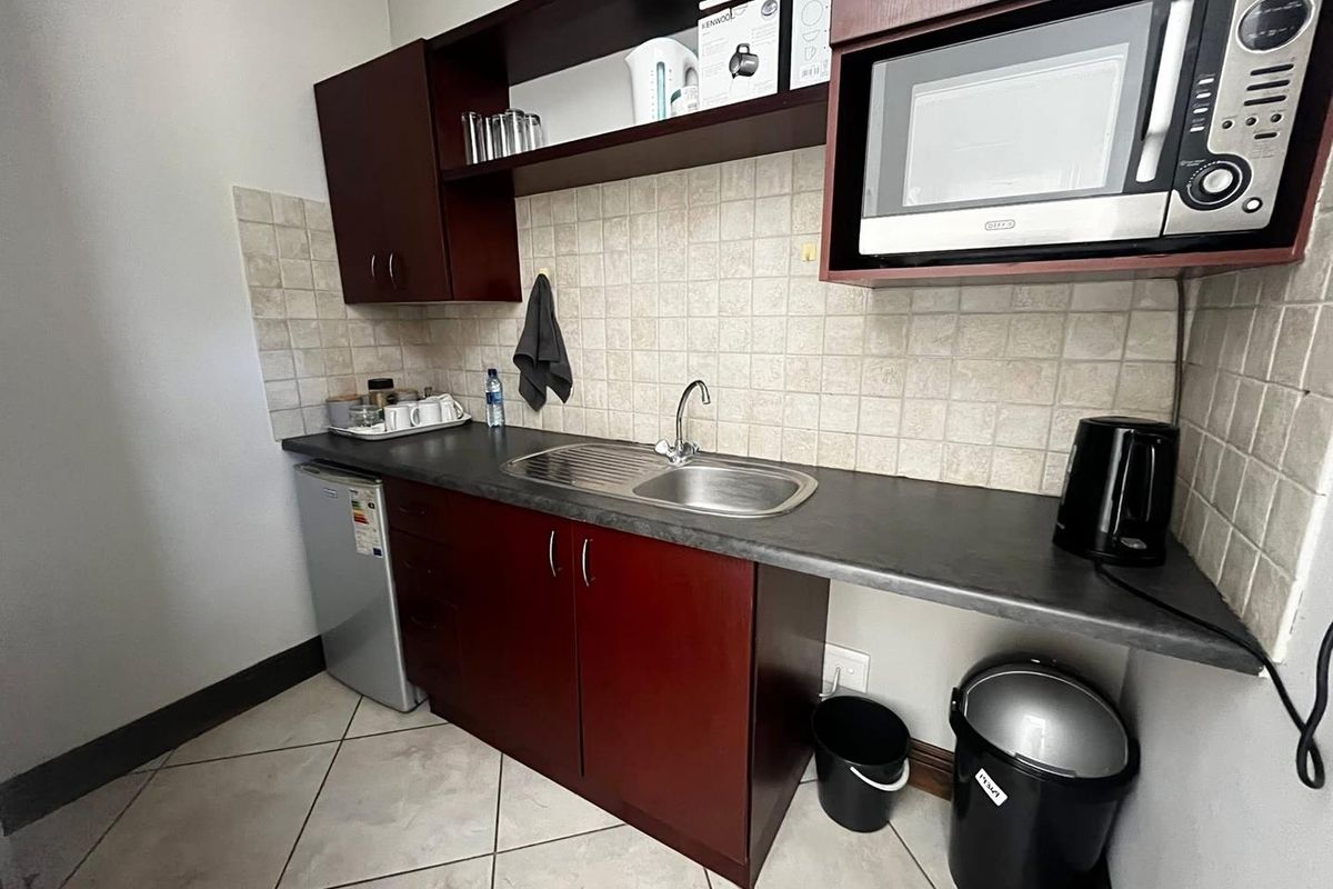 A compact kitchenette featuring dark wood cabinetry, a stainless steel sink, tiled backsplash, and a built-in microwave, suitable for office or small business use.