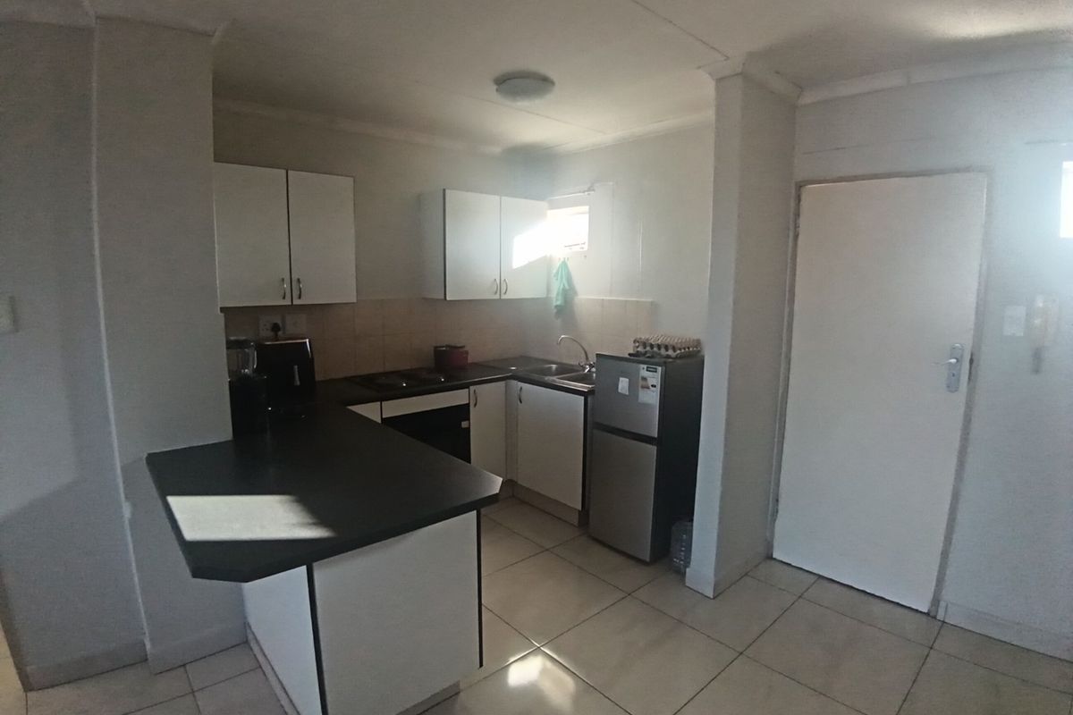 A functional kitchen featuring white cabinetry, dark laminate countertops, tiled flooring, and built-in cooking appliances, offering a practical layout for daily use.
