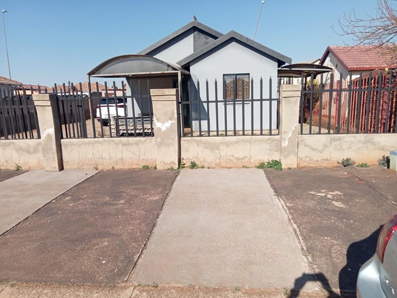 Front view of a detached house featuring a concrete driveway, metal perimeter fencing, and a covered carport area.