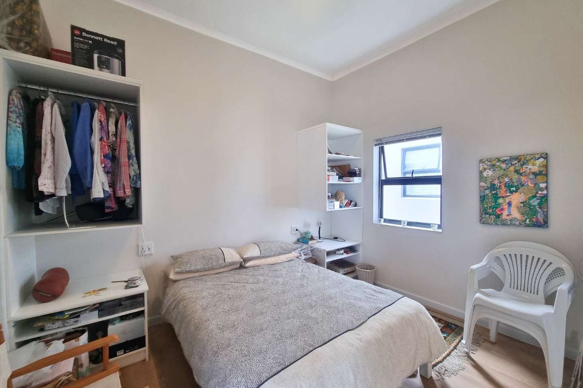 A functional bedroom featuring built-in shelving and wardrobe storage with laminate flooring and a window providing natural light.