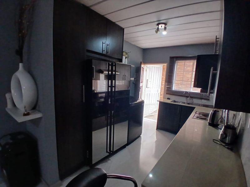 A functional kitchen featuring dark cabinetry, integrated appliances, a stainless steel sink, and tiled flooring with direct access to an exterior door.