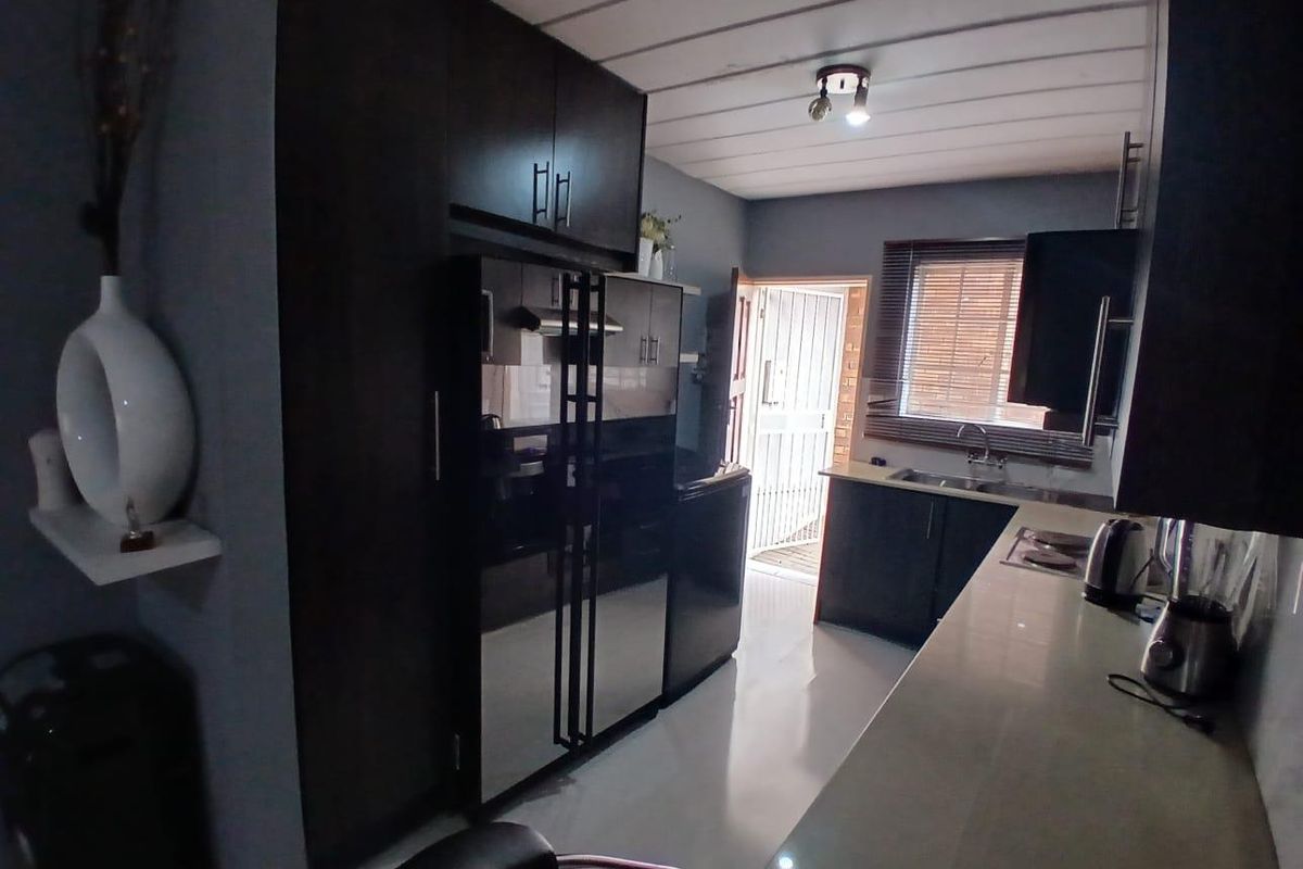 A functional kitchen featuring dark cabinetry, integrated appliances, a stainless steel sink, and tiled flooring with direct access to an exterior door.
