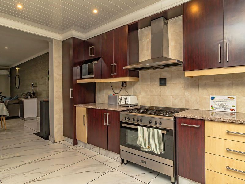 A well-maintained kitchen featuring dark wood cabinetry, granite countertops, a gas stove with extractor fan, and modern tiled flooring.