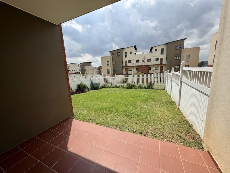 A private rear garden featuring a tiled patio area and a well-maintained lawn enclosed by a white picket fence.