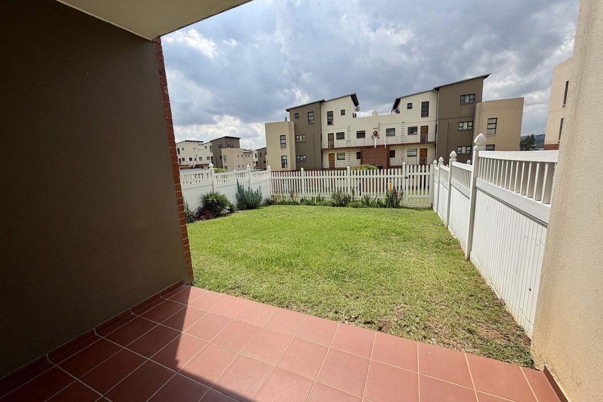 A private rear garden featuring a tiled patio area and a well-maintained lawn enclosed by a white picket fence.