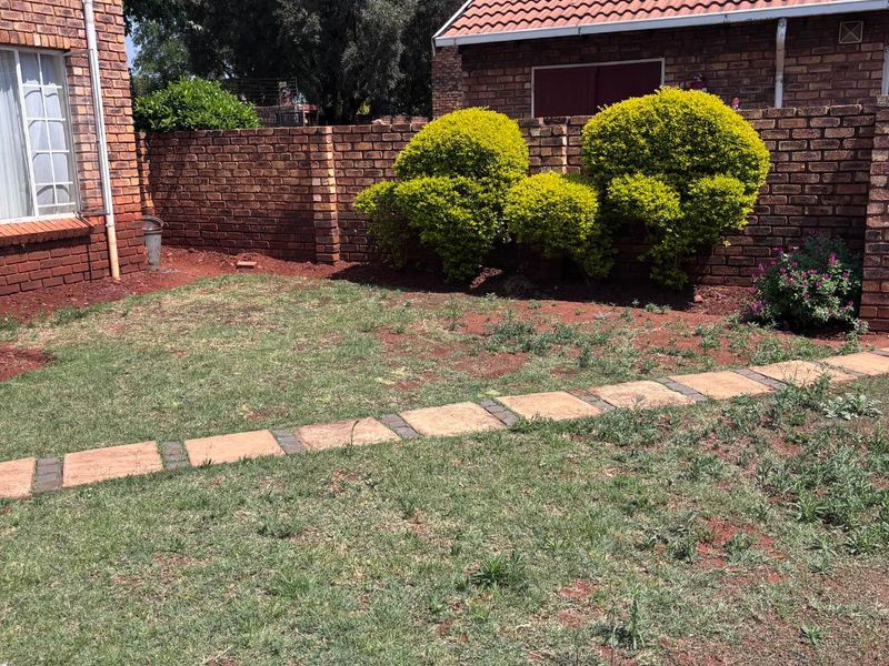 A private rear garden area featuring a brick boundary wall, a paved walkway, and established shrubs.