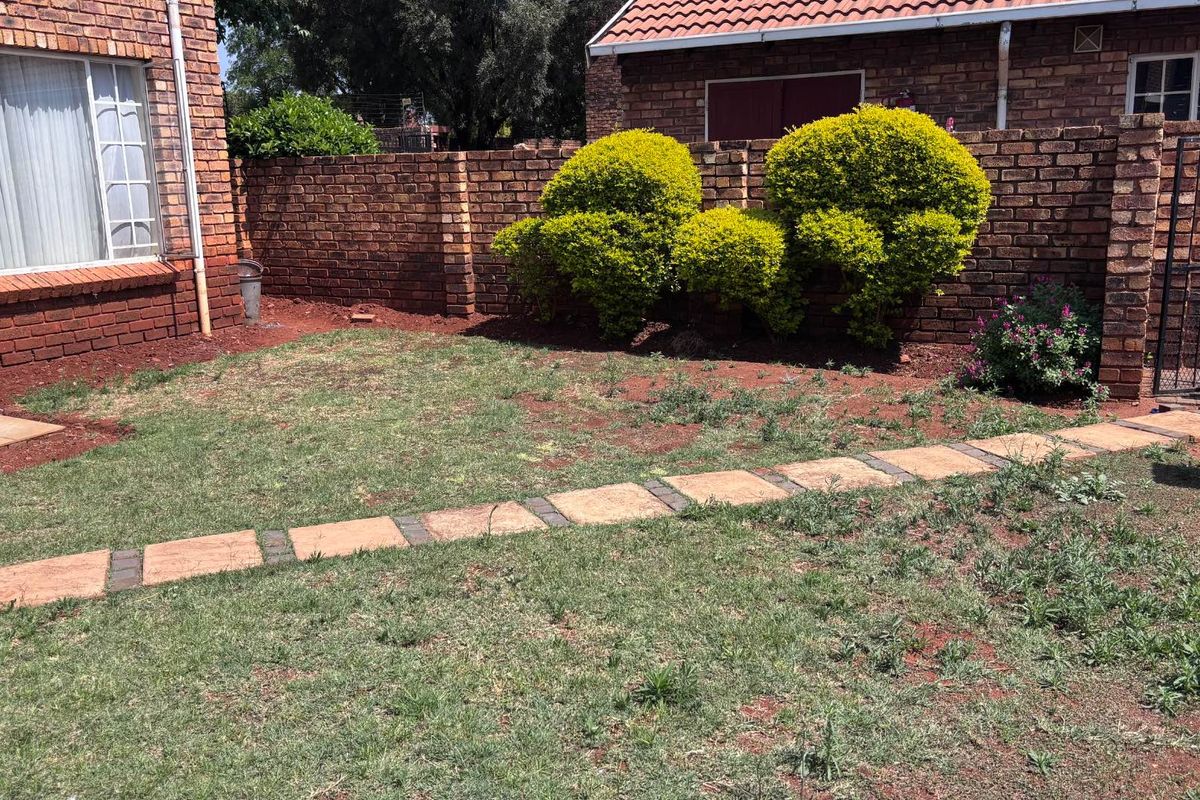 A private rear garden area featuring a brick boundary wall, a paved walkway, and established shrubs.