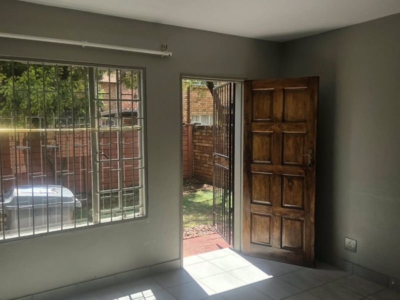 An empty living room featuring tiled flooring, security bars on the windows, and direct access to the rear garden through a wooden door.
